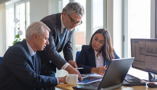 Concentrated colleagues watching statistic charts and talking about work. Professional senior managers and young assistant preparing business plan. Teamwork, management and partnership concept